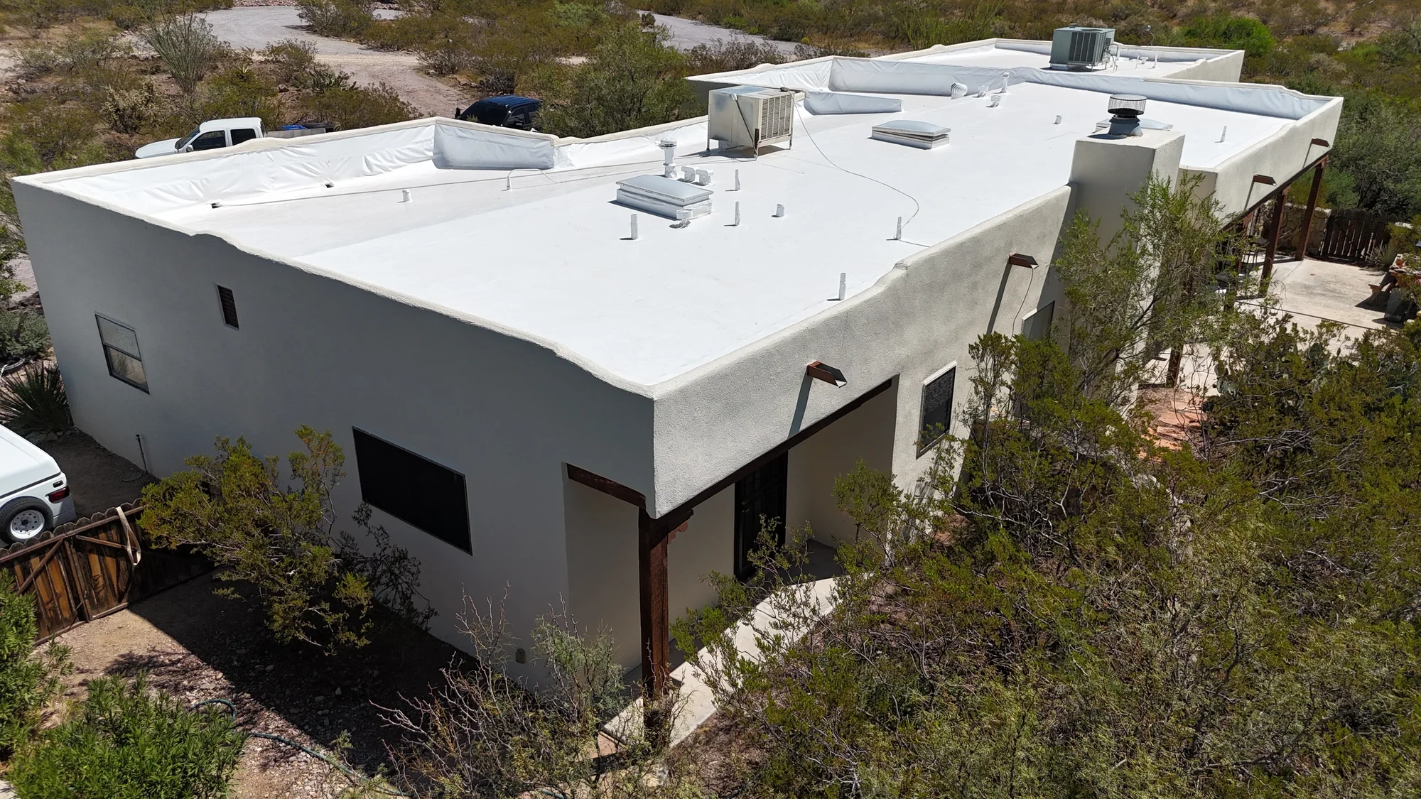 Aerial view of a gray stucco home with a white flat roof, covered patio, and desert landscaping.