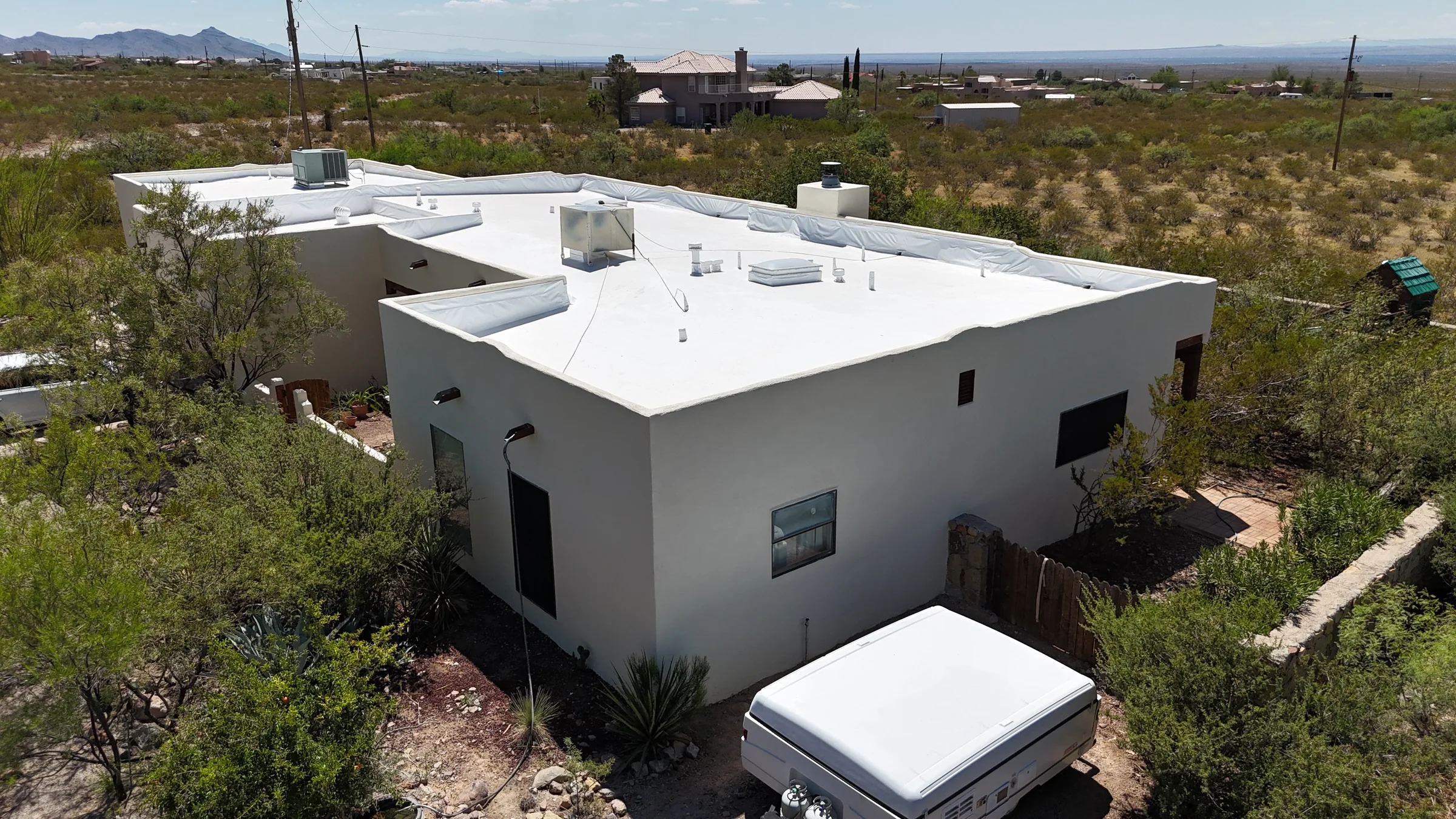 Aerial view of a light gray stucco home with a white flat roof and desert surroundings.