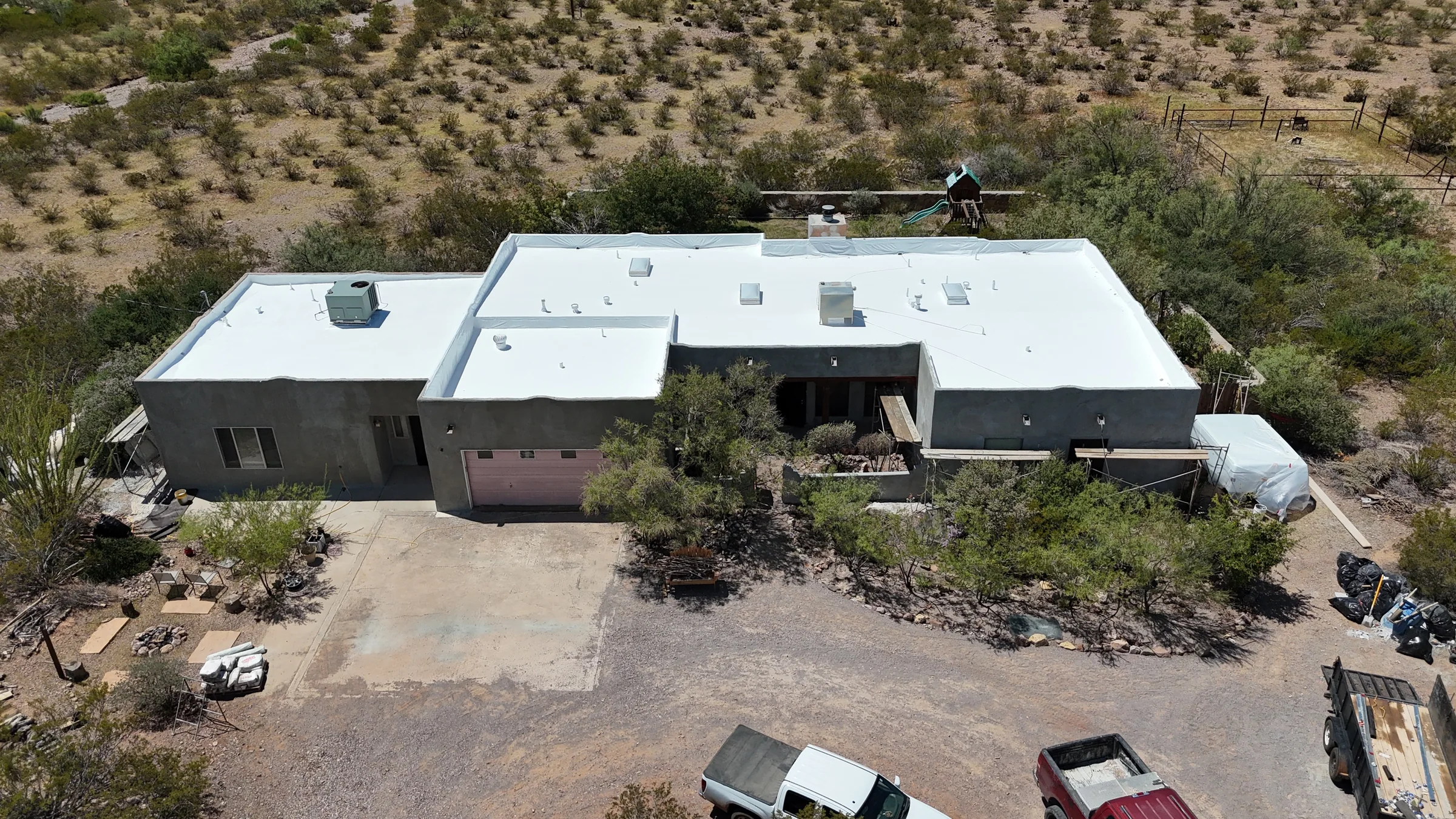Wide aerial view of gray stucco walls, a white flat roof and scaffolding around a residential exterior.