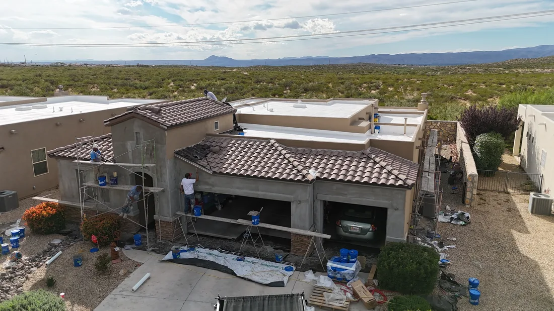 Aerial view of a tan stucco home with tile roofing, scaffolding, and exterior work materials.