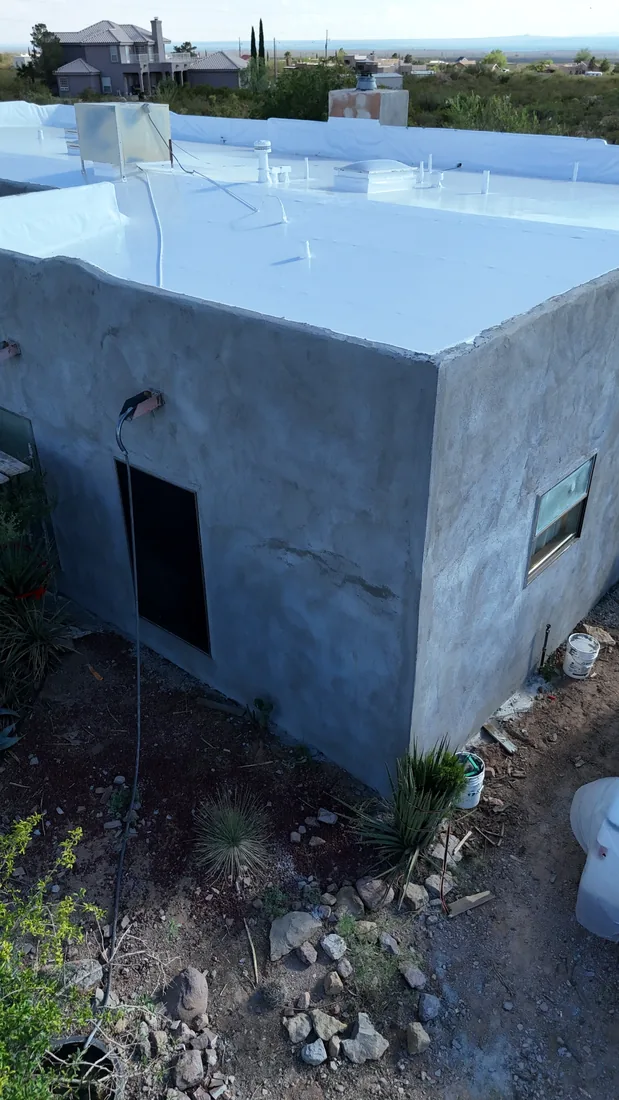 Angled view of unfinished gray stucco walls below a white flat roof, with a window and rock landscaping.