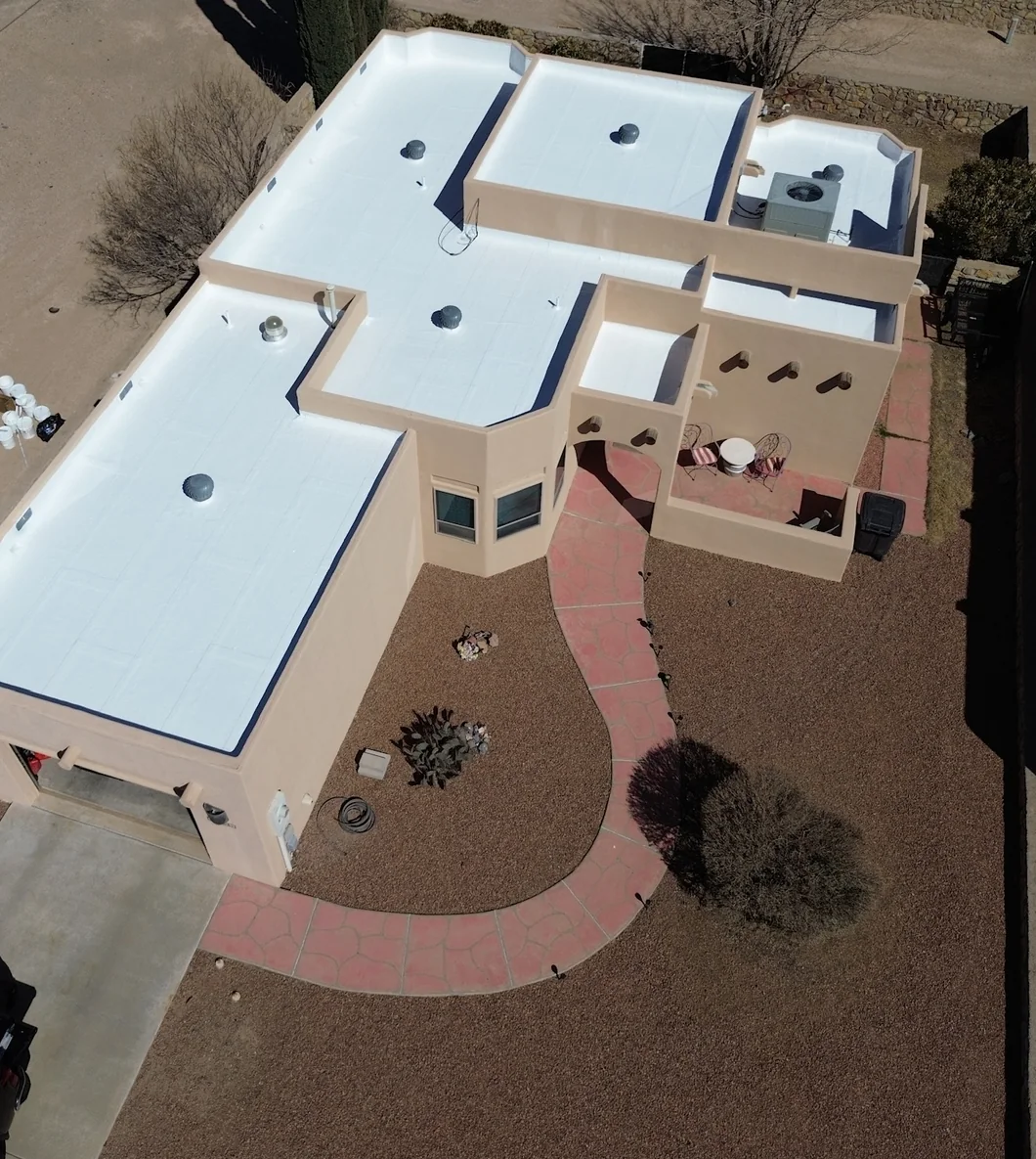 Aerial view of a pale tan stucco home with a white flat roof, enclosed courtyard and curved rose-colored walkway.
